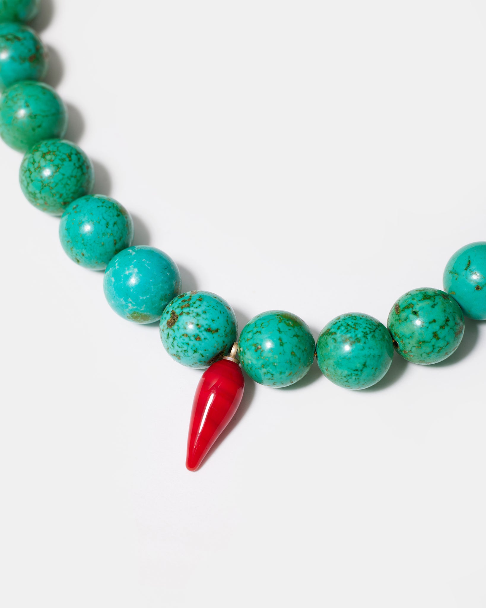 Close-up of turquoise bead necklace and red glass chili pendant